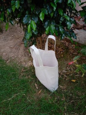 White Color Tote Bags Isolated on Green Grass Background. Non-woven bag with white Fabric handle loop Bag on Black Background. ECO-Friendly Polypropylene Bag. Biodegradable Shopping tote bag. Mockup bag. Reusable packaging.