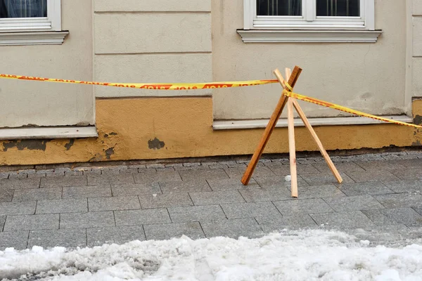 Snow and icicles falling down from a building rood, warning tape with words Stop