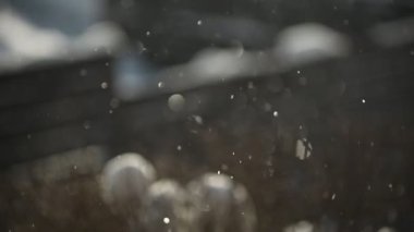 Kışın yavaş çekimde kar taneleri düşüyor. Bokeh ile kar taneleri güneş ışığına karşı çırpınıyor.