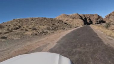 Beyaz araba Namibya 'nın güneyindeki Namibya dağlarında tozlu bir yolda ilerliyor..