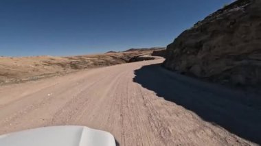 Beyaz araba Namibya 'nın güneyindeki Namibya dağlarında tozlu bir yolda ilerliyor..