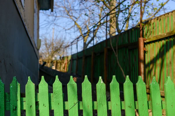 Green fence with blurry old house in background — Stock Photo, Image