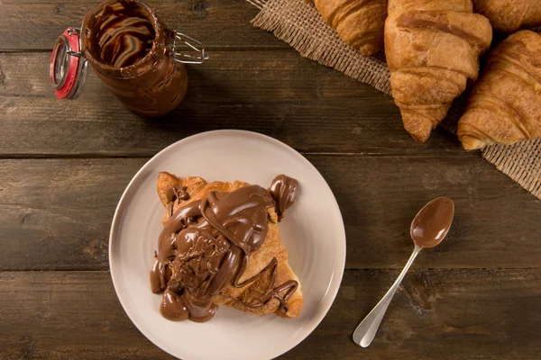 Snídani croissant s čokoládou na rustikální pozadí — Stock fotografie