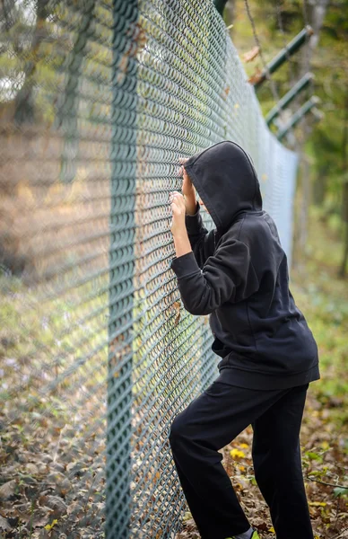 Wire fence standing in front of hooded young — Stock Photo, Image