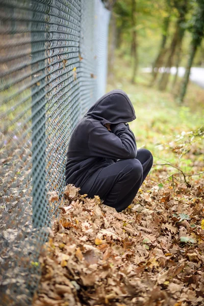 Wire fence sitting in front of hooded young — Stock Photo, Image