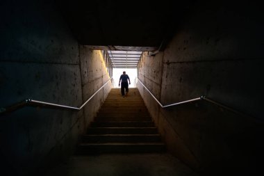 Adam karanlık ortamda merdivenden ışığa doğru yürüyor..