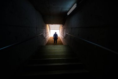 Adam karanlık ortamda merdivenden ışığa doğru yürüyor..