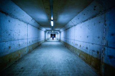 Bir adam yeraltı geçidinde yürüyor. Karanlık bir ortam..