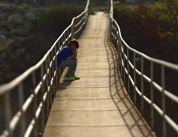 Самотній хлопчик сидить на підвісному мосту — стокове фото