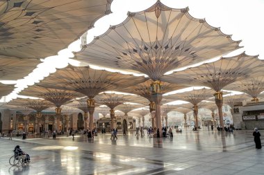 Pilgrims walk underneath giant umbrellas at Nabawi Mosque clipart