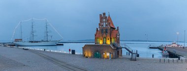 Stralsund limanının panoramik manzarası. Tarihi pilot evi ve yelkenli gemisi Gorch Fock kış sabahının erken saatlerinde