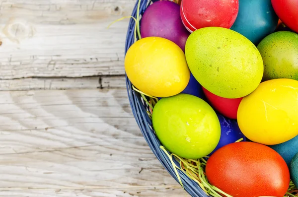 Цветные пасхальные яйца в корзине на деревянном фоне — стоковое фото