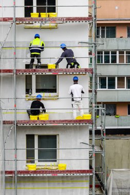 Dört işçi yenilemek için apartmanın ön cephesine dekoratif alçı uyguluyor.