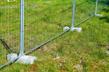 Beton ağırlık askılarına monte edilmiş geçici galvanize çelik çit parçaları eskrimin dengesini koruyor
