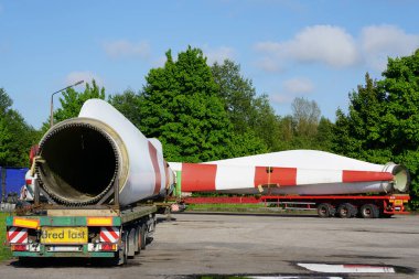 Bir kamyon manzarası, yaz günü otoparkta geniş rüzgar türbini parçaları olan düşük yüklenmiş bir yarı römork.