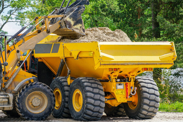 yellow front loader loads the sand into the dump truck