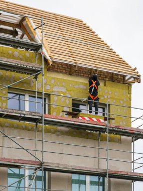 İnşaat işçisi, çok katlı bir eve mineral yünlü yünlü yalıtım döşeme iskelesinde emniyet kemeri takıyor.