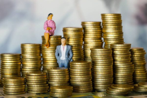 Миниатюрная деловая женщина и бизнесмен стоят и сидят на пачках монет, символизирующих финансы, богатство, инвестиции, экономический рост и процветание