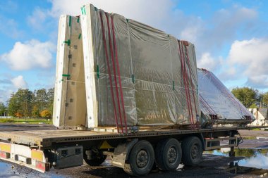 Prefabrik beton paneller koruyucu plastiğe sarılı ve bir inşaat lojistik sahasında bir kamyon römorkuna sıkıca bağlanmış.
