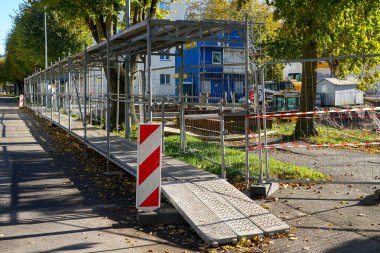 Sonbahar boyunca şehir merkezindeki etkin bir inşaat alanı boyunca metal iskeleler ve güvenlik bariyerleriyle geçici yaya geçidini güvence altına alın.