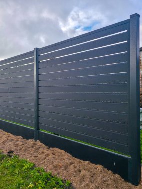 Mimari, mahremiyet ve tasarımı temsil eden, panellerde yağmur damlaları ve bulutlu bir gökyüzü arkaplanı olan yeni, koyu gri metal bir çitin yakın çekimi