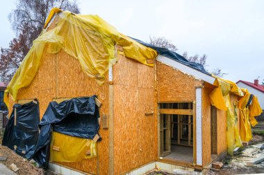 Yalıtım ve hava koruması için sarı ve siyah plastik çarşaflarla kaplı yapım aşamasındaki ahşap ev.