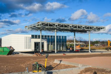 Çelik bir tepe örtüsü, modern hizmet binası ve şantiye çevresinde aktif inşaat çalışmalarının yer aldığı yeni bir benzin istasyonu tamamlanmak üzere.