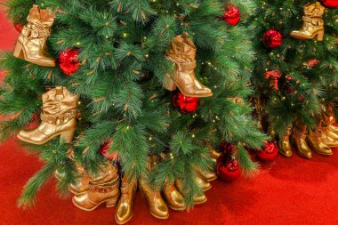 Altın çizmeler ve kırmızı takılarla süslenmiş bir ayakkabı mağazasındaki Noel ağacı, moda temalı eşsiz bir bayram perakendecisi oluşturuyor.