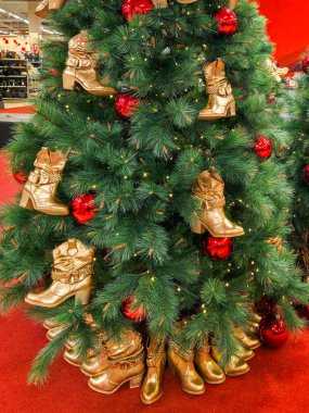 Altın çizmeler ve kırmızı takılarla süslenmiş bir ayakkabı mağazasındaki Noel ağacı eşsiz bir Noel gösterisi yaratıyor.