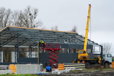 İnşaat işçileri sanayi kurulumu sırasında çelik çerçeve yapısına makas kaldırma ve vinç ile sandviç duvarı panelleri monte ediyorlar.