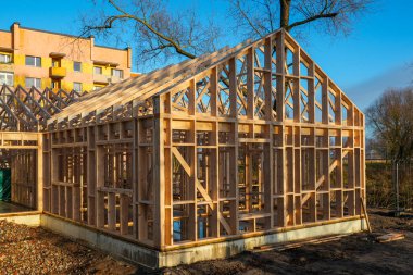 Çatı kirişleri ve duvar çivileri ile inşaat halindeki ahşap çerçeveli ev, kentsel inşaat alanında modern ahşap mimari.