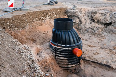 Bir inşaat sahasına yerleştirilen plastik yeraltı drenaj inceleme odası kısmen toprağa gömülüp turuncu bir boruya bağlanıyor.