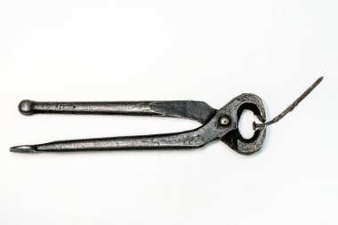 Paslı çiviyi tutan eski demirci kıskaçları, beyaz arka planda izole edilmiş. Eski el yapımı metal aletler aşınmayı, tarihi ve işçiliği gösteriyor.