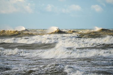 Şiddetli Baltık Denizi dalgaları dramatik bir güçle kabarır ve çarpar. Güçlü bir kıyı fırtınası sırasında bulutlu bir gökyüzünün altında beyaz köpük ve deniz püskürtüsü oluşturur.