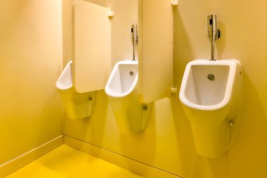 Üç beyaz seramik pisuvarın olduğu temiz modern tuvalet. Parlak sarı bir iç kısımda gizlilik ayırıcıları var.