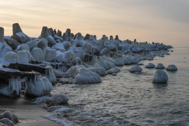 Letonya, Liepaja 'daki Baltık Denizi kıyısı boyunca buzla kaplı donmuş beton kırma suyu, deniz kenarında sakin bir kış günbatımı sırasında