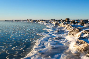 Liepaja limanındaki Baltık Denizi kışı manzarası. Letonya, buz gibi kıyı şeridi, donmuş kayalar ve açık mavi gökyüzü altındaki deniz buzu.