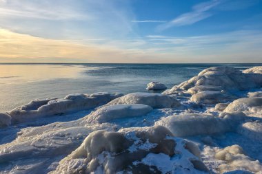 Donmuş buz oluşumları ve kar, Liepaja, Letonya 'daki Baltık Denizi kıyı şeridini kaplayarak günbatımında huzurlu bir kış deniz manzarası yaratıyor..