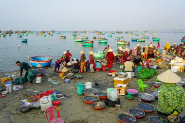 Mui Ne, Vietnam- 22 Mart 2025: Yerel halk deniz kenarı pazarında renkli balıkçı tekneleri gün doğumunda taze balıklarla dönerken, sahil geleneği