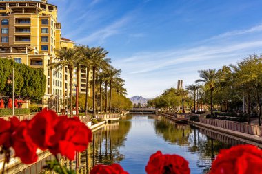 Arizona 'daki Old Town Scottsdale' in rıhtım ve alışveriş bölgesi boyunca uzanan gündüz kanalı manzarası. Odaklanamayan kırmızı çiçeklerle çerçevelenmiş.