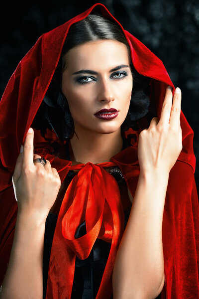 Beautiful brunette woman in black old-fashioned dress and red cloak in the thicket of the magic forest. Gothic style. Fashion.
