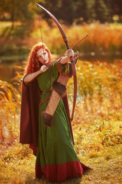 Orta Çağ 'ın güzel kızıl saçlı okçusu gölün yanında duruyor. Kelt kültürü. Hayal dünyası..