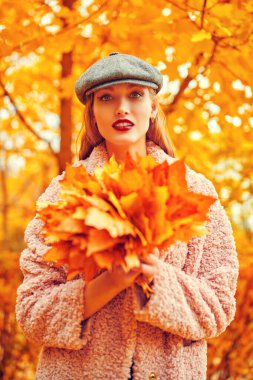 Güzel genç bir kadın elinde bir buket sarı akçaağaç yaprağıyla sonbahar parkında yürüyor. Mutlu sonbahar havası. 