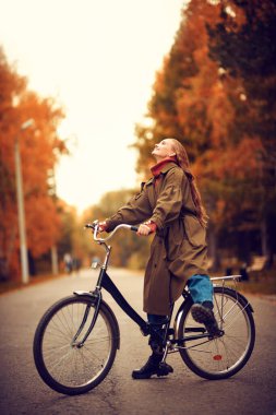 Mutlu kız güzel bir sonbahar parkında bisiklet sürüyor. Sonbahar havası.
