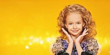 Cadılar Bayramı kutlaması. Cadı kostümü giymiş güzel kıvırcık saçlı şirin küçük kız kameraya gülümsüyor. Sarı arka planda stüdyo portresi. Boşluğu kopyala.