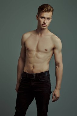 Gri-yeşil arka planda mükemmel kaslı vücudu olan yakışıklı bir genç adamın portresi. Spor ve vücut geliştirme. Erkeklerin güzelliği ve sağlığı.