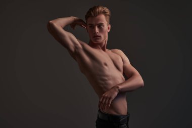 Koyu gri arka planda mükemmel kaslı vücudu olan yakışıklı bir genç adamın portresi. Spor ve vücut geliştirme. Erkeklerin güzelliği ve sağlığı.