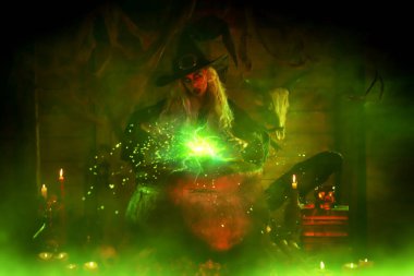 Korkunç yaşlı cadı, sihirli yeşil ışıkla çevrili kazanın üzerine büyü yapıyor. Cadılar Bayramı. Korkunç hikayeler..