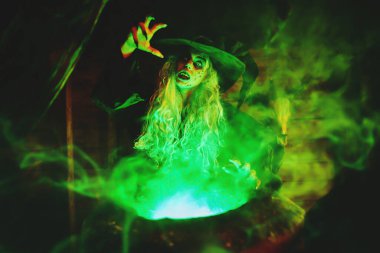 Korkunç yaşlı cadı, sihirli yeşil ışıkla çevrili kazanında iksir yapıyor. Cadılar Bayramı. Korkunç hikayeler..