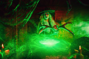 Korkunç yaşlı cadı sihirli yeşil ışıkla çevrili asanın yardımıyla kazanda iksir yapıyor. Cadılar Bayramı. Korkunç hikayeler..